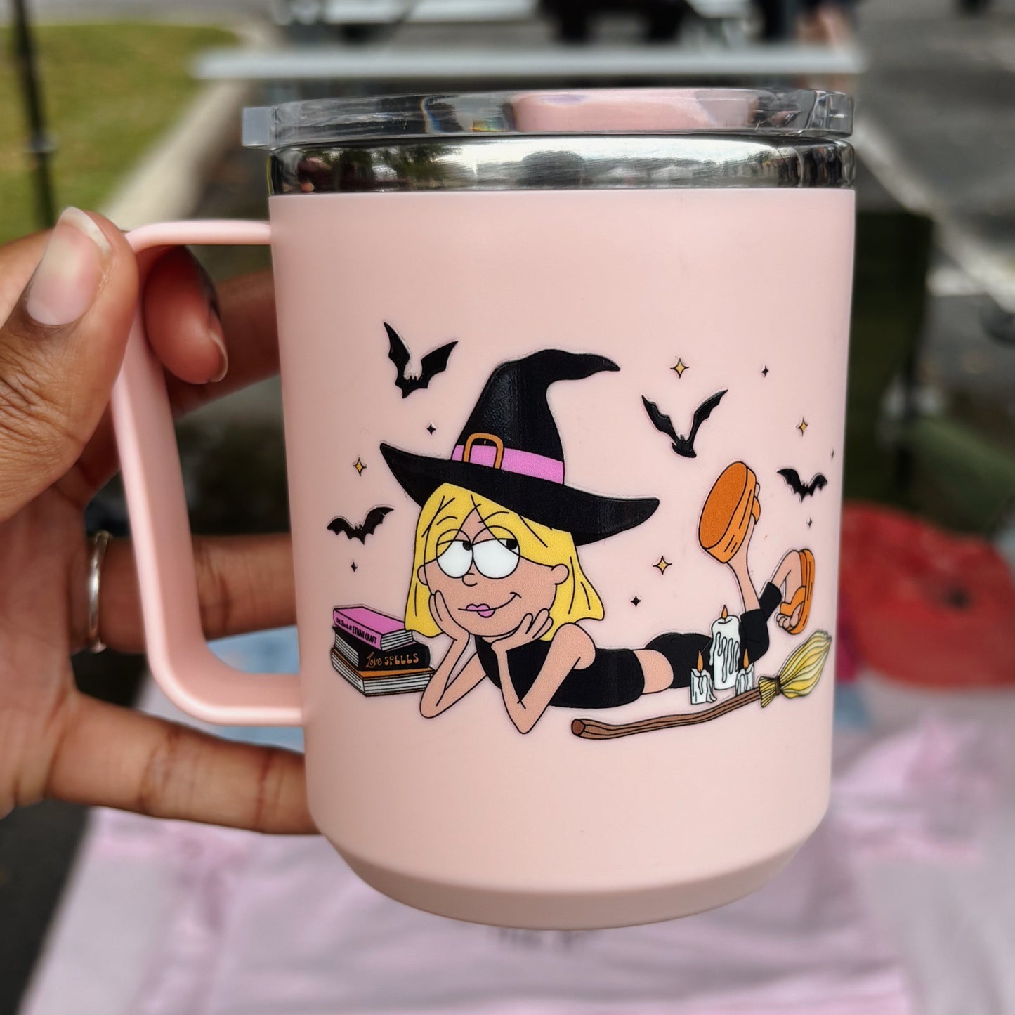 Pink mug with a witch design held by a hand, blurred outdoor background