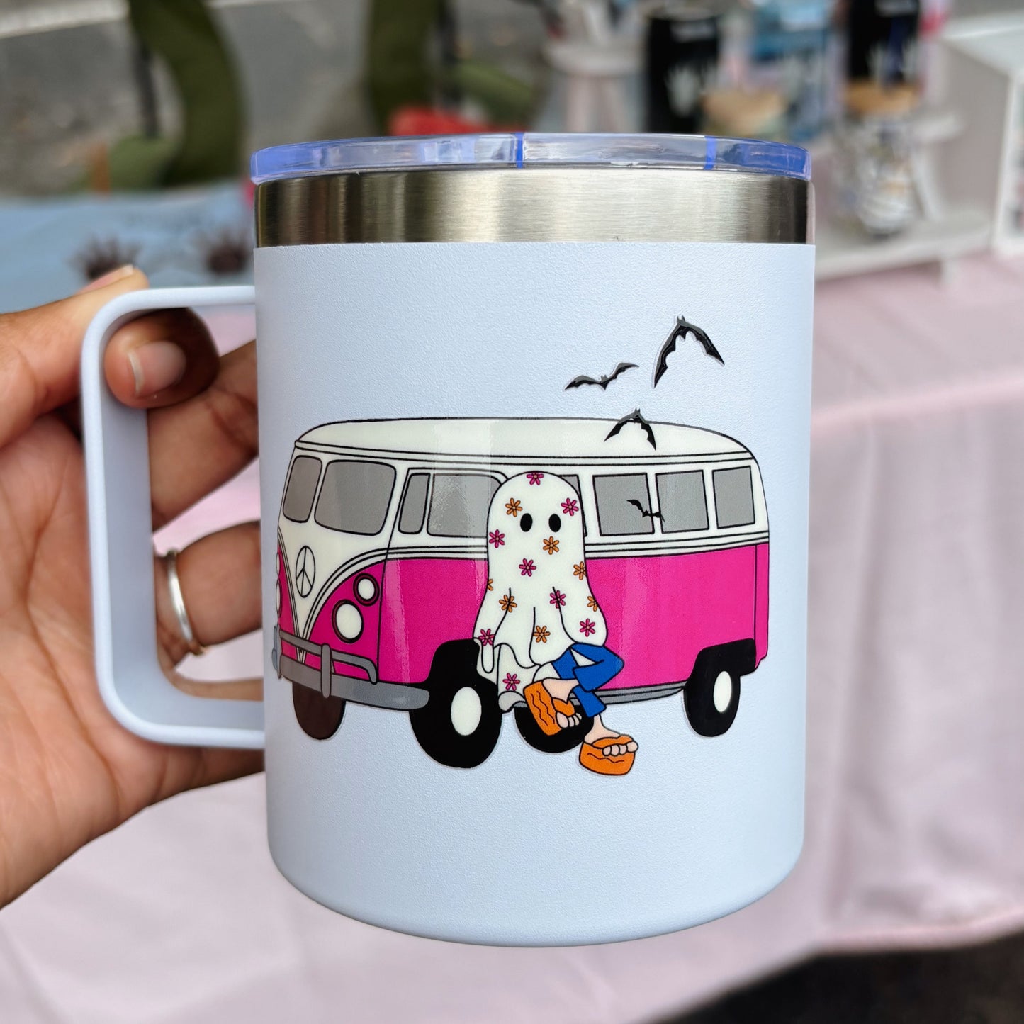 Mug with a pink van and cartoon character design held by a hand.