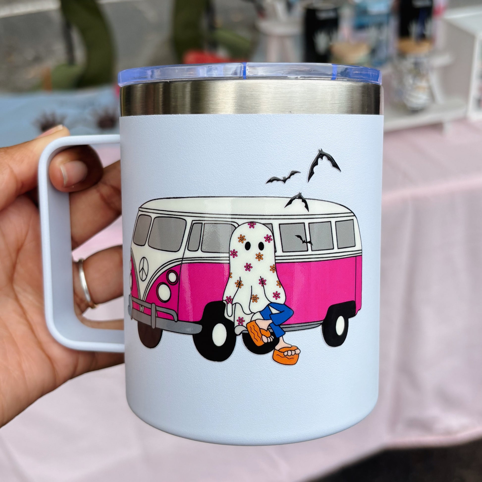 Mug with a pink van and cartoon character design held by a hand.
