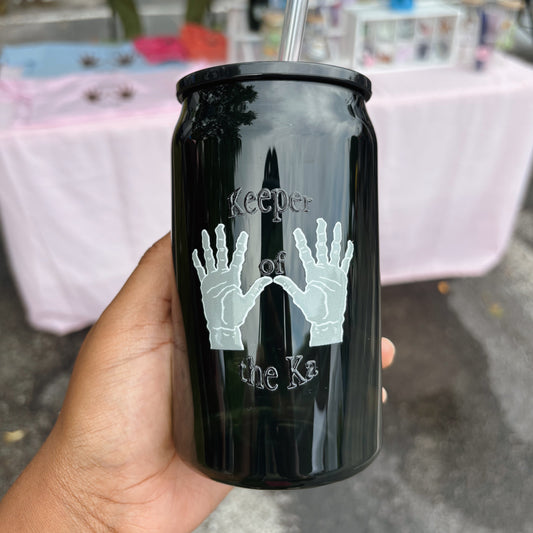 Black tumbler with hands and text held by a hand in an indoor setting.
