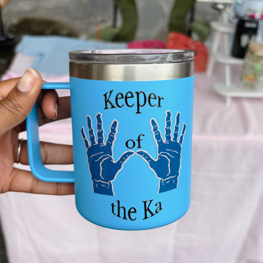 Blue mug with 'Keeper of the Ka' text and hand designs held by a person.